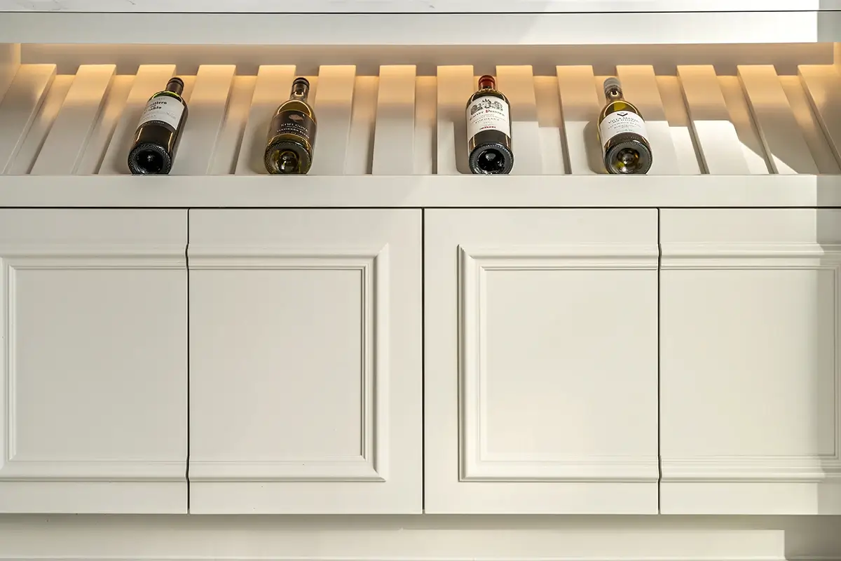 Wine bottles displayed in illuminated storage above traditional panelled kitchen cabinets
