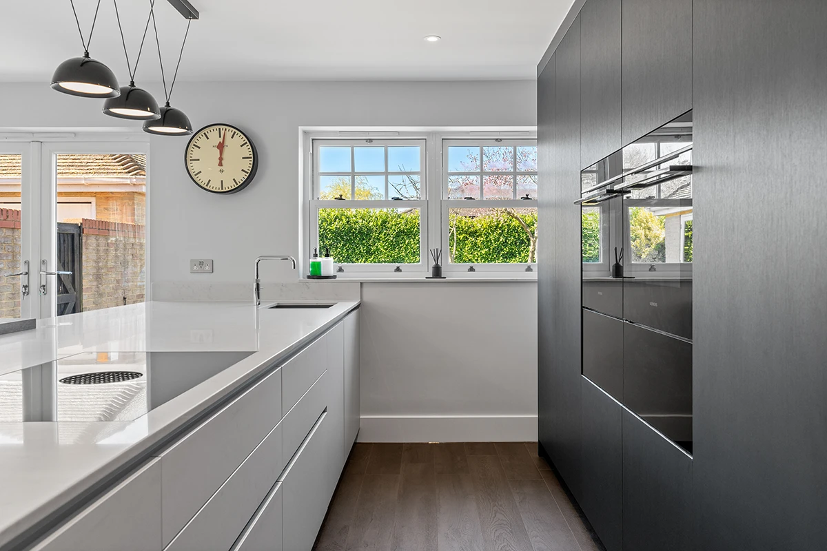 Galley kitchen with grey cabinets, white worktops and a window above the sink