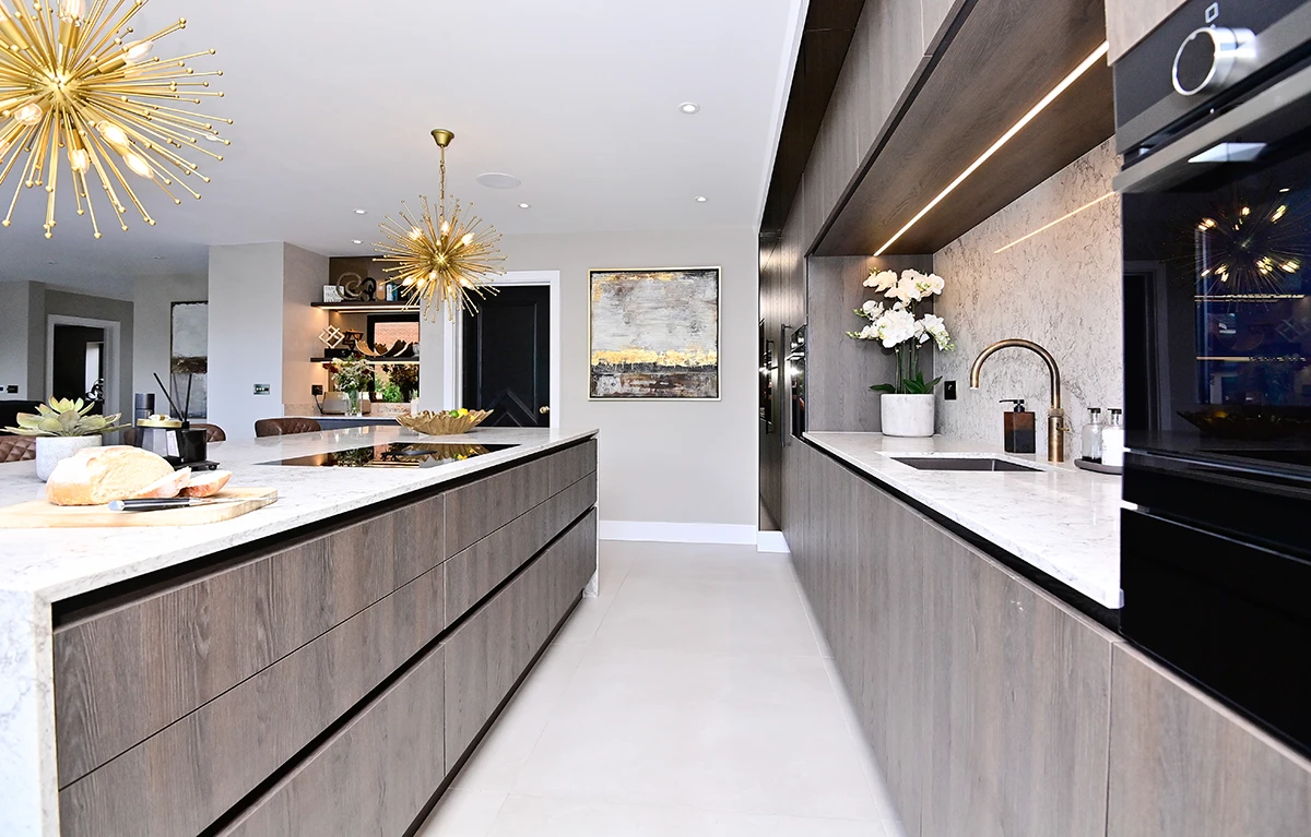 Long view of a white kitchen island and dark wood cabinets with integrated ovens