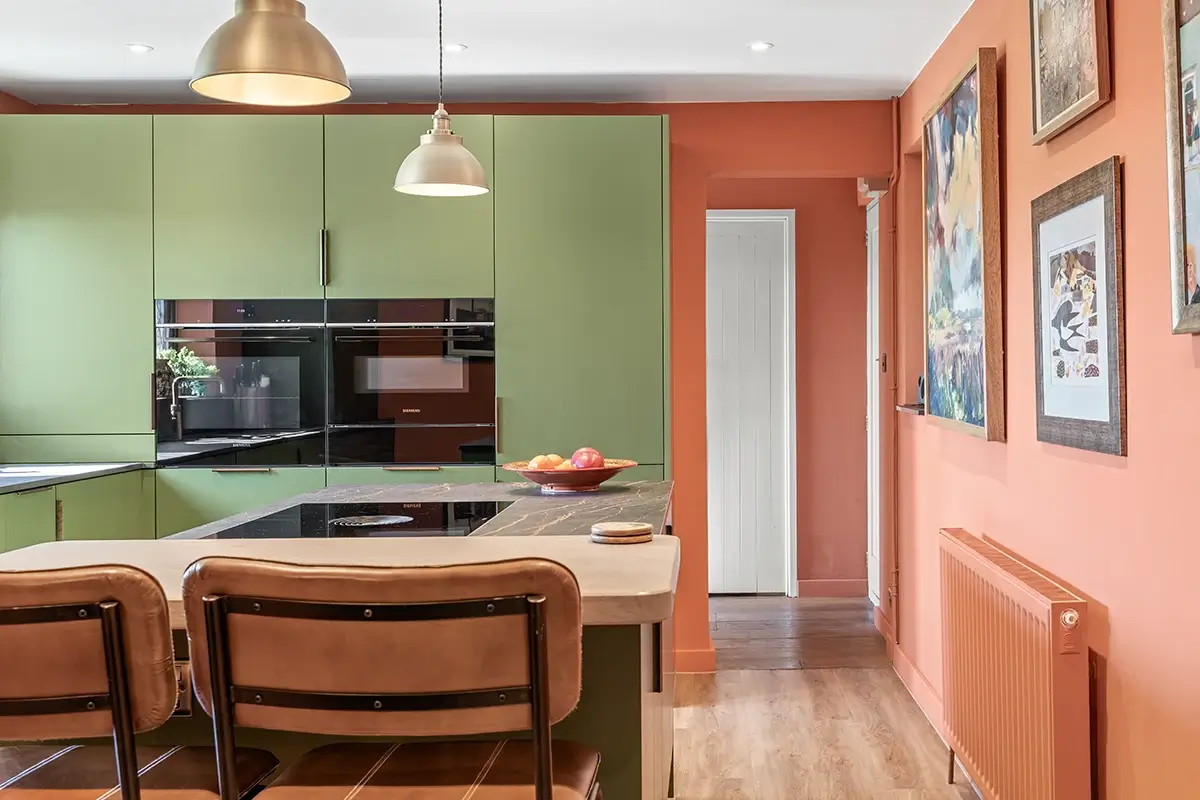 Green kitchen cabinetry with warm terracotta walls and a central island