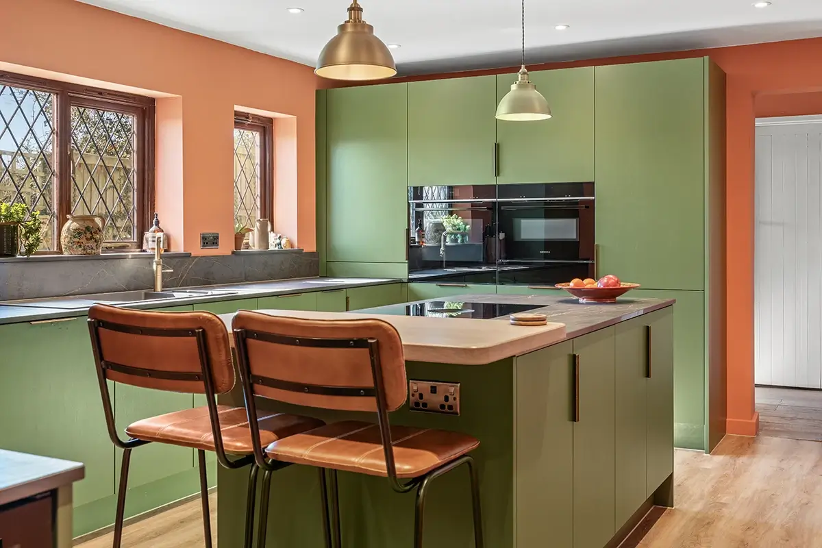 Green kitchen island with bar stools, pendant lights and terracotta walls